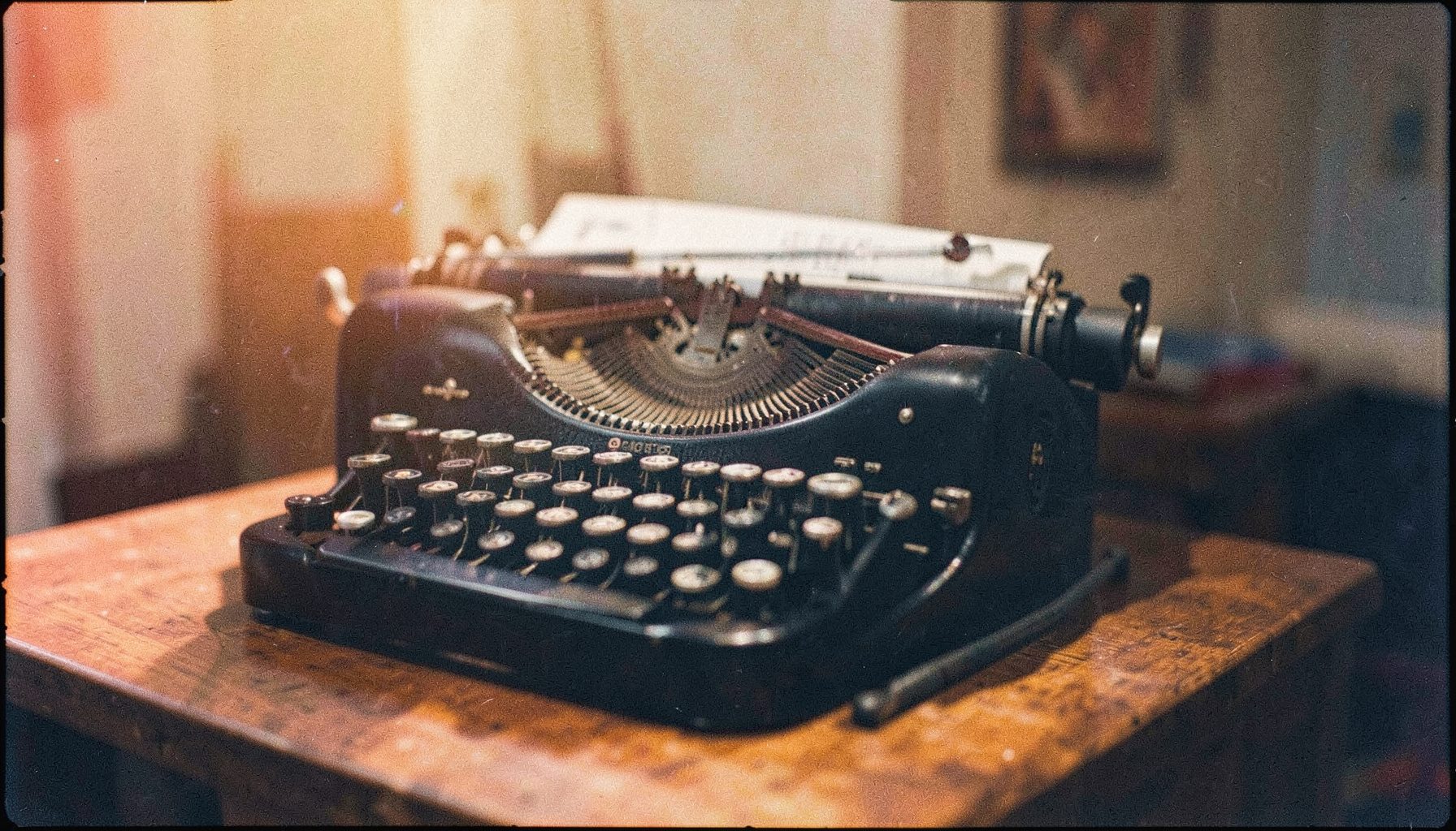Analog film photograph of a vintage typewriter on a wooden desk, soft warm afternoon light, visible grain and muted orange and navy tones, contemplative mood.