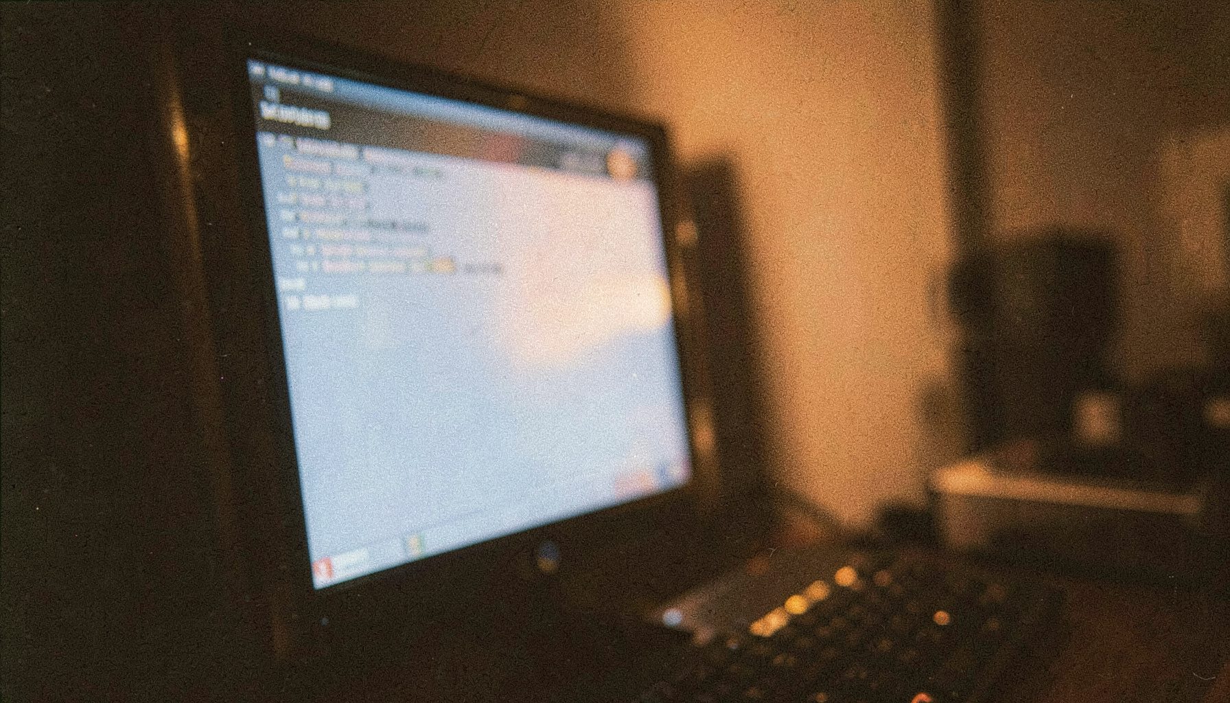 Abstract close-up of a computer screen glowing with soft blue and orange light in a dim room, grainy analog film texture, moody technology atmosphere